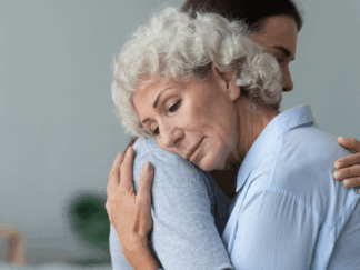 Two women hugging looking sad.