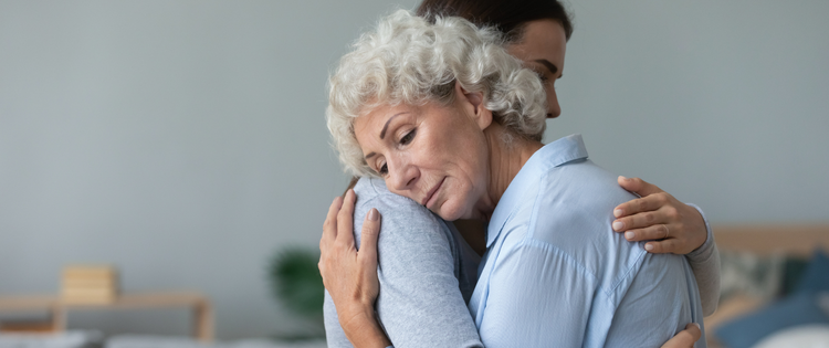 Two women hugging looking sad.